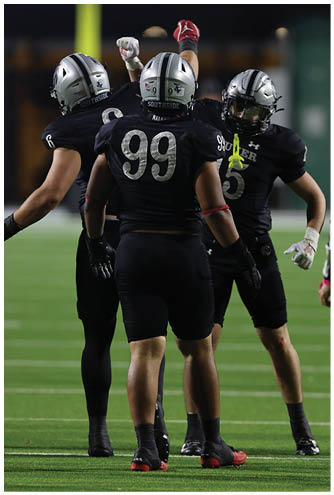 Two people wearing black football uniforms and helmets are on a field, with one facing the camera and the other facing away. Description generated by AI