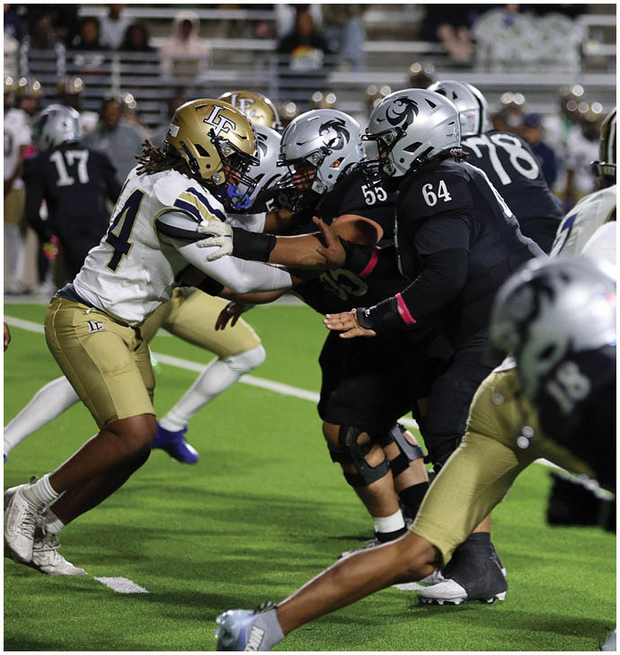 Players in football uniforms are actively engaged in a play on a green field during a game. Description generated by AI