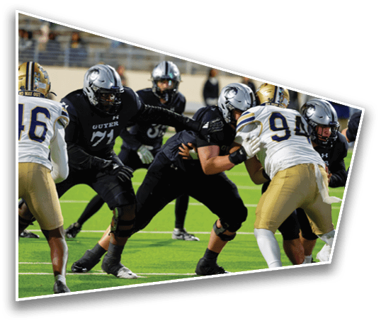 Players in football uniforms from two opposing teams are engaged in a play on a green field with one team wearing black and the other wearing white and gold. Description generated by AI