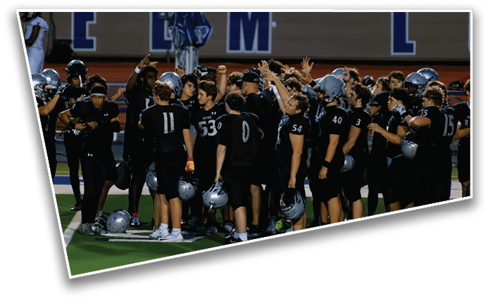 A group of people wearing black sports uniforms and holding helmets are gathered closely together on a field, raising their hands in a team huddle. Description generated by AI