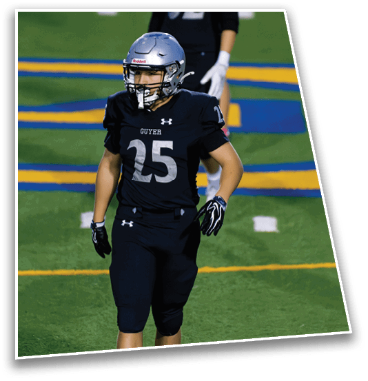 A person wearing a black football uniform with the number 25 and a silver helmet is standing on a green football field with blue and yellow markings. Description generated by AI