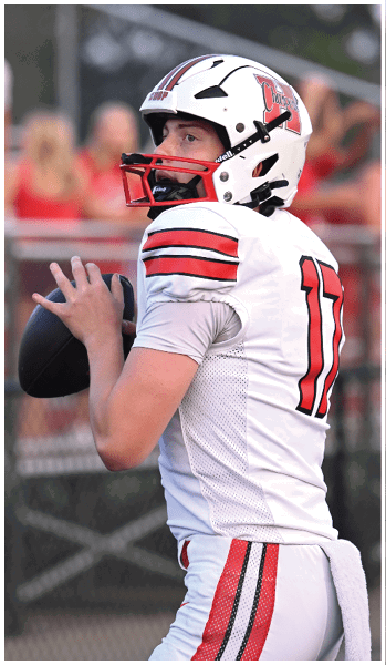 A person wearing a white football helmet with red and black stripes and a white jersey is preparing to throw a football. Description generated by AI