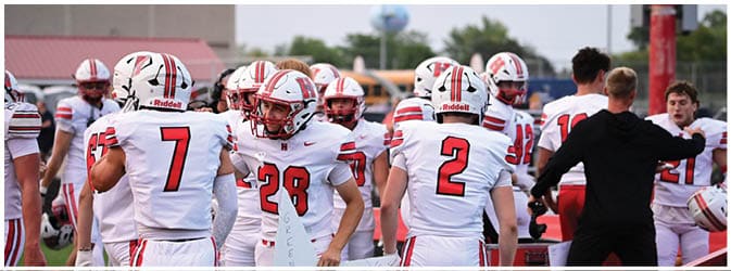 People in football uniforms stand on a field with one holding a large white star-shaped sign. Description generated by AI