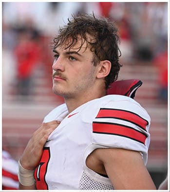 A person with short, wet hair and a mustache is looking to the right against a blurred background with red and white colors. Description generated by AI