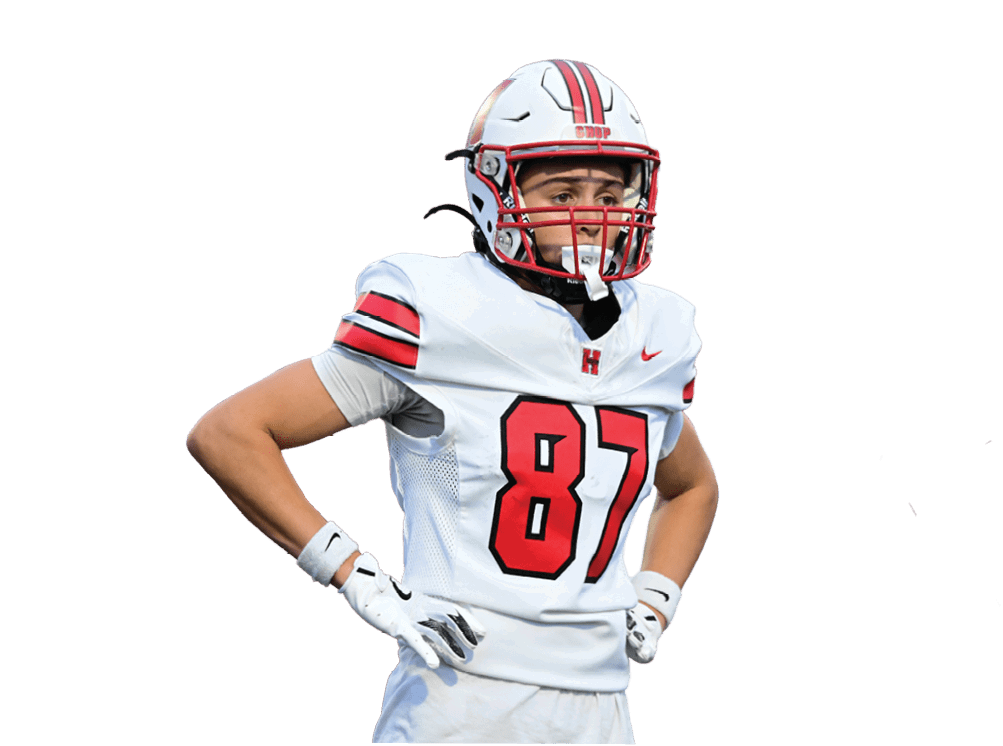 A person wearing a white football uniform with the number 87 and a helmet stands with hands on hips against a white background. Description generated by AI
