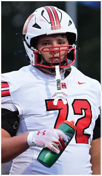 A person wearing a white football uniform with the number 72 and a helmet is holding a green water bottle. Description generated by AI