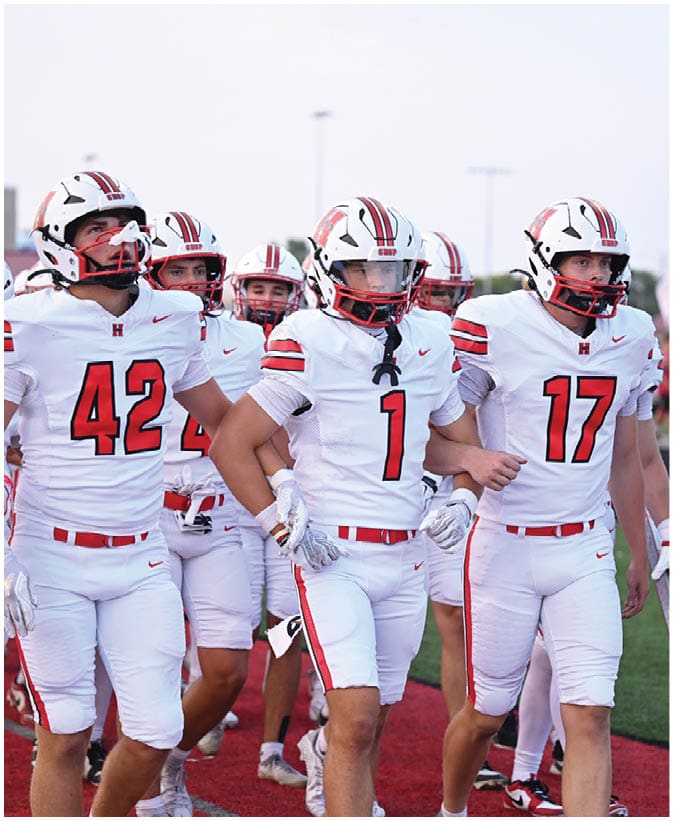 A group of people wearing white football uniforms with red and black stripes are walking together on a field. Description generated by AI