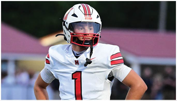 A person wearing a white football uniform with the number one and a white helmet is looking to the side on a field with blurred background. Description generated by AI