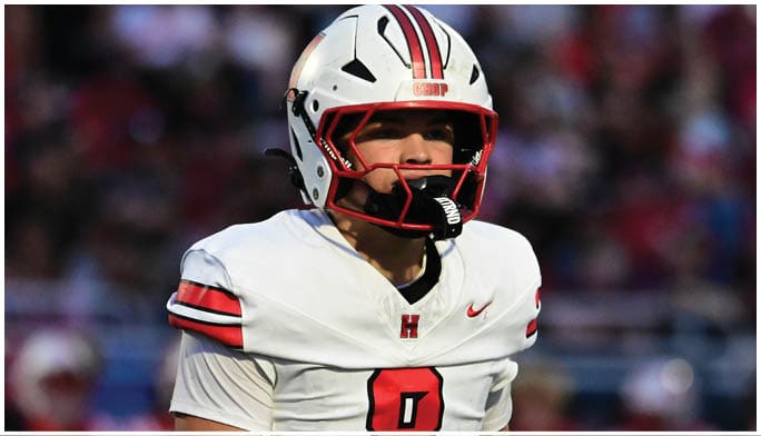 A person wearing a white football uniform with the number 8 and a white helmet stands on a field with a blurred crowd in the background. Description generated by AI
