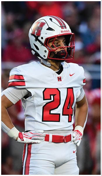 A person wearing a white football uniform with the number 24 and a white helmet stands with hands on hips on a football field. Description generated by AI