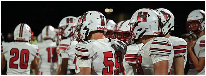 People wearing white football uniforms with red and black stripes are gathered on a field, some facing away and others standing side by side. Description generated by AI