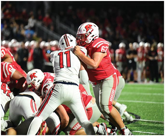 A group of people wearing football uniforms are engaged in a play on a well-lit field with a crowd in the background. Description generated by AI