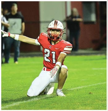 A person in a red football uniform with the number 21 is reaching out with one arm extended on a grassy field during a game. Description generated by AI