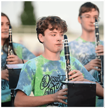 Three people wearing tie-dye shirts are playing clarinets outdoors, with one person in the foreground focused on their instrument. Description generated by AI