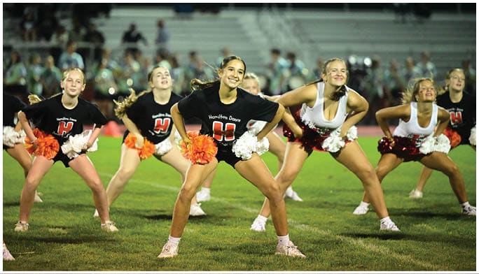 A group of people in cheerleading outfits are performing a routine on a sports field with pom-poms in hand. Description generated by AI