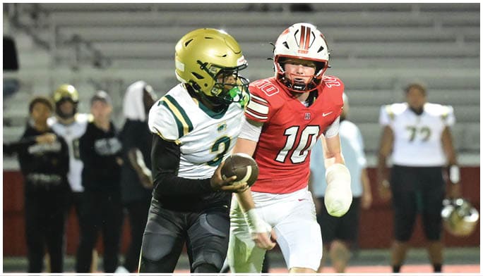 Two football players in helmets and uniforms are actively engaged on the field with one holding the ball and the other closely defending. Description generated by AI