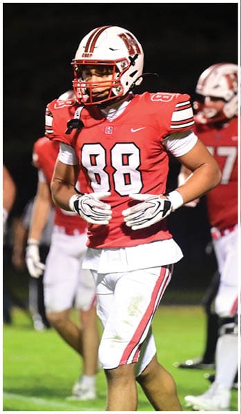 Several people wearing red and white football uniforms are standing and walking on a grassy field at night. Description generated by AI
