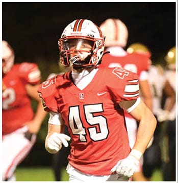 A person wearing a red football uniform with the number 45 is running on a field with other players in the background. Description generated by AI