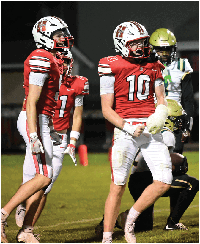 Three people in red and white football uniforms stand on a field at night with one person wearing a cast on their right arm and two people in black and gold uniforms in the background. Description generated by AI