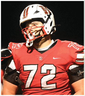 A person wearing a red football jersey with the number 72 and a white helmet is standing on a field at night. Description generated by AI