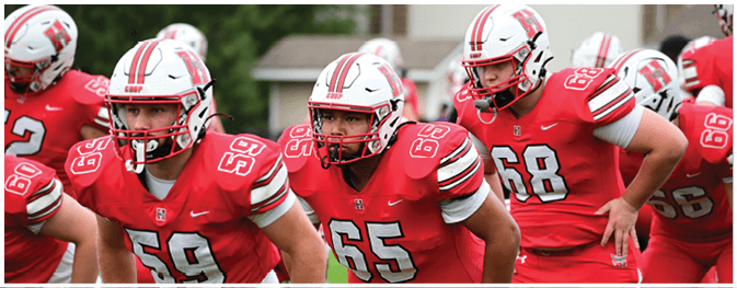 People wearing red football uniforms and helmets are running together on a field. Description generated by AI