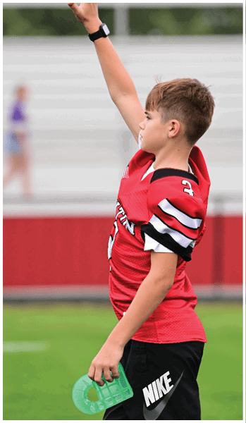 A person wearing a red sports jersey and black shorts is raising one arm while holding a green water bottle in the other hand on a sports field. Description generated by AI