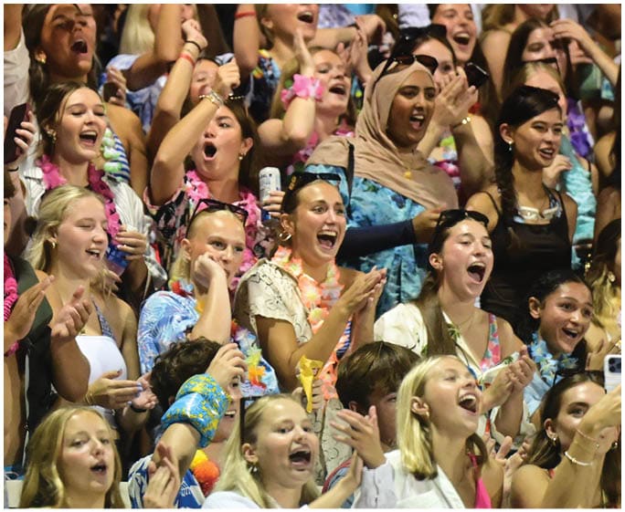 A large group of excited people wearing colorful clothing and leis are cheering and clapping enthusiastically at an event. Description generated by AI