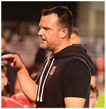 A person wearing a black hoodie with white drawstrings and a small red and white patch on the chest is shown in a close-up side view. Description generated by AI