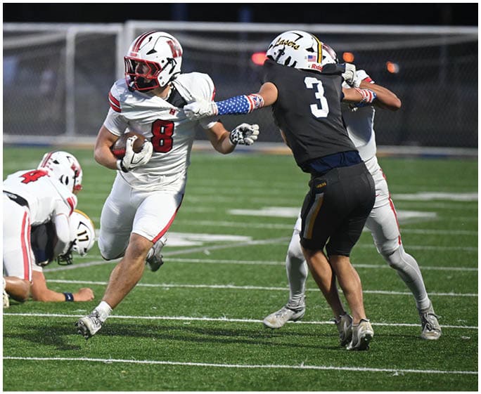A person in a white football uniform with the number 8 is running with the ball while another person in a white uniform with the number 4 is tackling an opponent on a football field. Description generated by AI