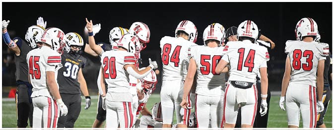 People wearing football uniforms are gathered on a field at night with some raising their hands. Description generated by AI