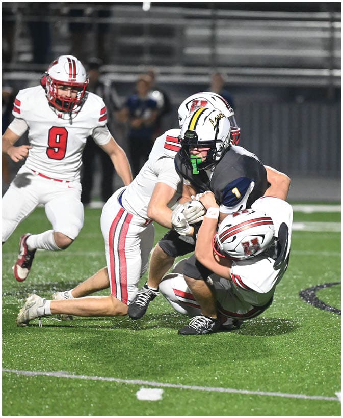 A group of people in football uniforms are engaged in a tackle on a green field during a game. Description generated by AI
