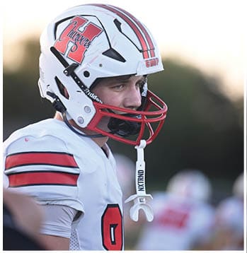 A white sports helmet with red and black stripes and the word “CHOP" written on the back is shown against a blurred outdoor background. Description generated by AI