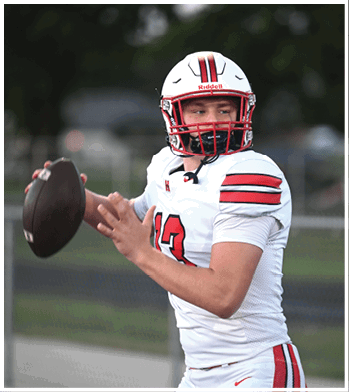 A person wearing a white football uniform with red and black stripes and a helmet is preparing to throw a football. Description generated by AI