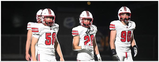 Five people wearing white football uniforms with red and black stripes are standing on a field at night. Description generated by AI