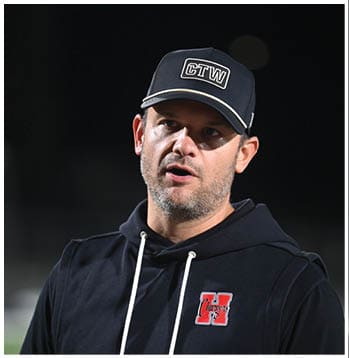 A person wearing a black hoodie with a red logo and a black cap with white lettering is speaking outdoors at night. Description generated by AI