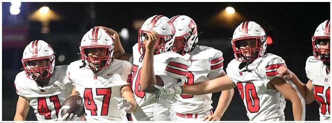 Four people in white and red football uniforms are running on a field, with one holding a football. Description generated by AI