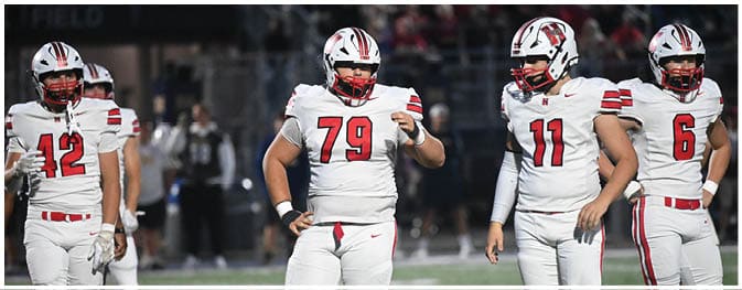 Three people wearing white football uniforms with red and black accents stand on a field during a game. Description generated by AI