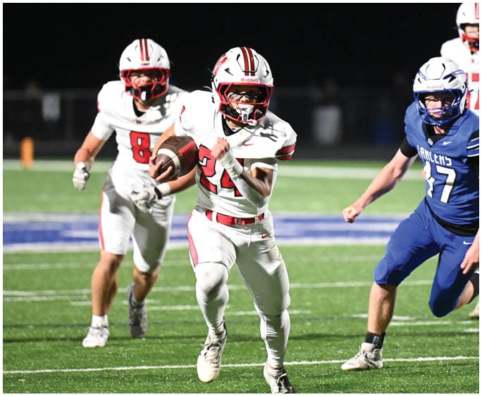 People in football uniforms are actively running on a well-lit field during a nighttime game. Description generated by AI
