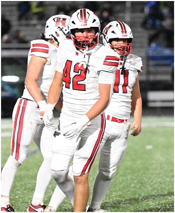 Three people wearing white football uniforms with red and black stripes stand on a field during a game. Description generated by AI
