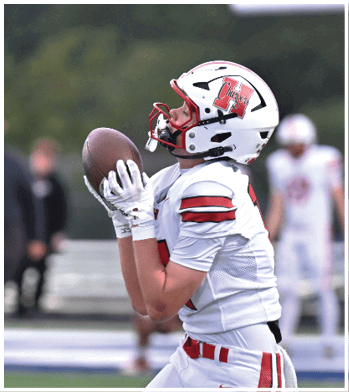 A person wearing a white football helmet with a red faceguard and a logo that says Chargers is holding a football close to their face while looking upward. Description generated by AI