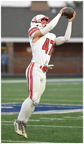 A person wearing a white football uniform with red stripes and the number 47 is jumping to catch a football on a field. Description generated by AI