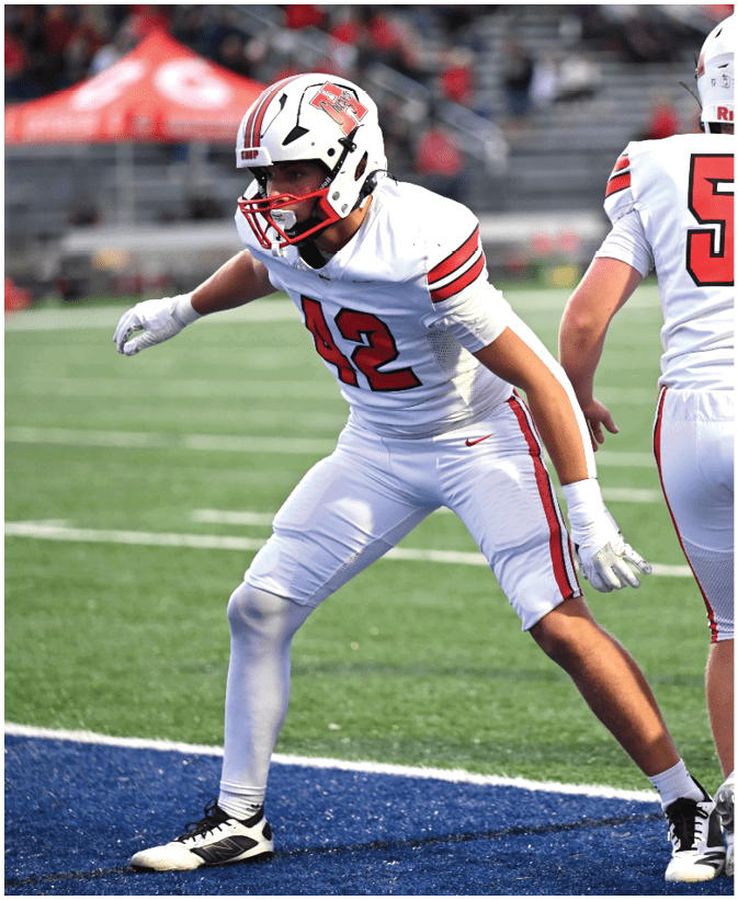 Two people in white football uniforms with red and black stripes are standing on a field, one facing away wearing a helmet with the number 58 on the back. Description generated by AI