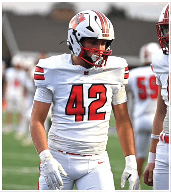 Two people wearing white football uniforms with red and black accents stand on a football field during a game or practice. Description generated by AI