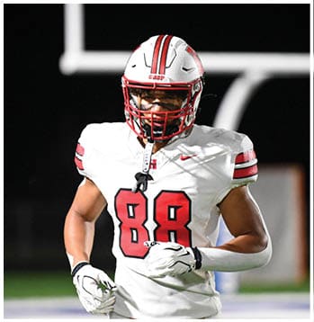 A person wearing a white football uniform with the number 88 in red is running on a football field at night. Description generated by AI