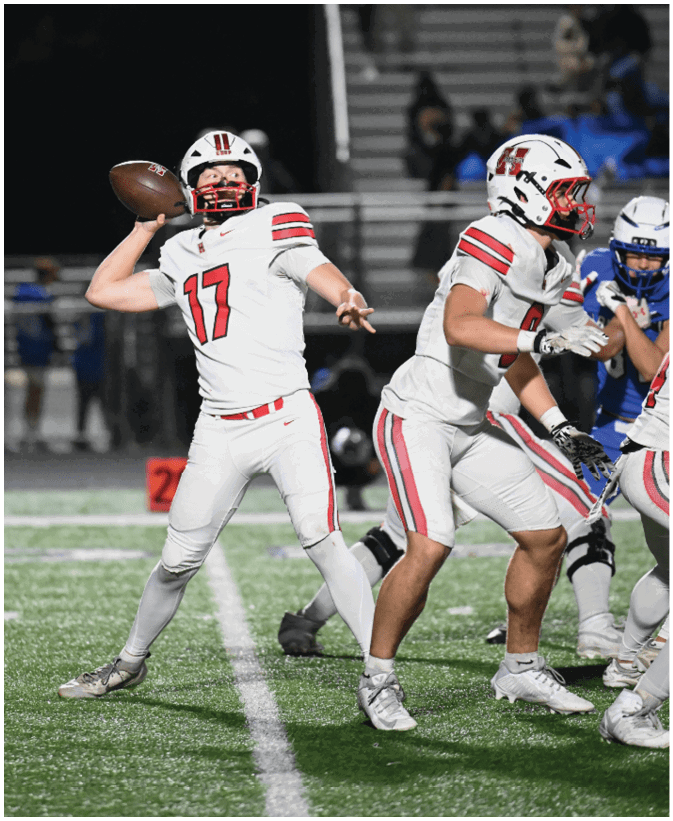 A person wearing a white football uniform with the number 17 is preparing to throw a football while another person in a similar uniform is positioned nearby on a football field during a game. Description generated by AI
