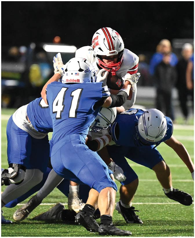 A group of people in football uniforms are engaged in a tackle on a grassy field during a nighttime game. Description generated by AI