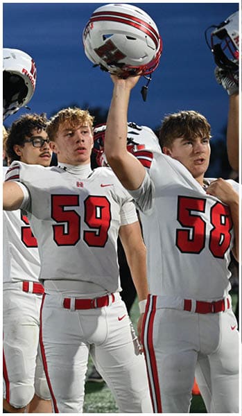 People in football uniforms with red and white colors stand in a line on a field with their arms raised. Description generated by AI