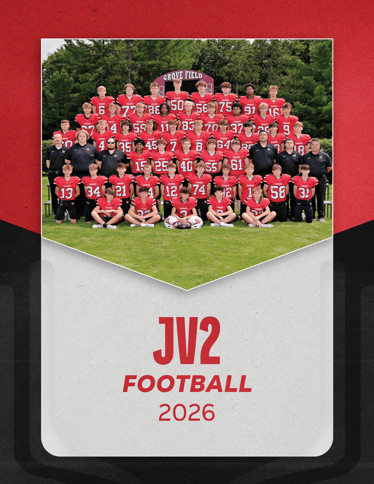 A large group of people wearing red and black football uniforms pose together on a grassy field with trees in the background and a sign that reads “JV2 Football 2026" below the photo. Description generated by AI