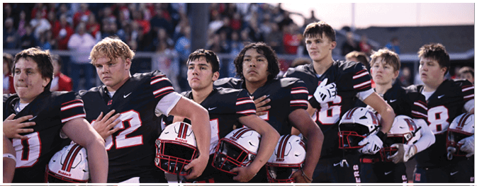 A group of people wearing black football uniforms with red and white stripes stand in a line holding white helmets with red and black details. Description generated by AI