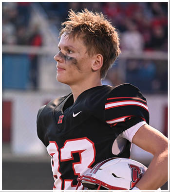 A person wearing a black football jersey with the number 83 and eye black is holding a white football helmet and looking to the side. Description generated by AI